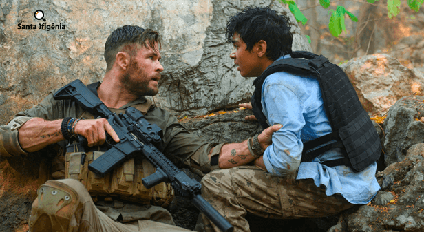 Chris Hemsworth com roupa de guerra, segurando o braço de um menino em Resgate